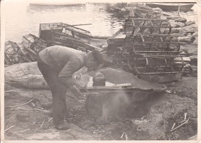 Oppvarming av tjære for tjæring av hummertener. Fotografi fra Spjærøy tatt på slutten av 1940- tallet/ begynnelsen av 1950- tallet. I bakgrunnen ses en stabel med vartener (sylindriske garntener). Fotografi utlånt av Jan Willy Ekeli.